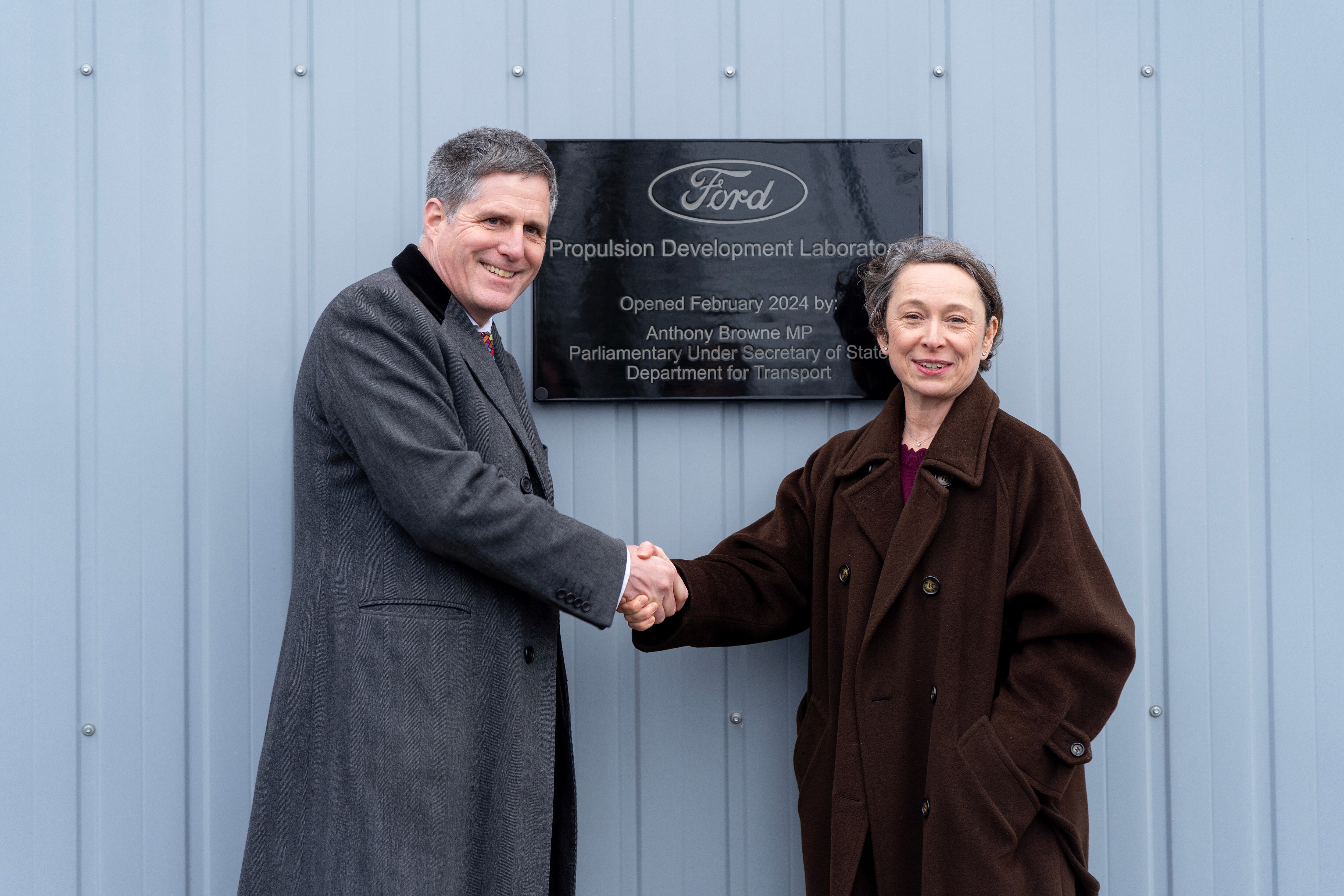 Two people shaking hands in front of plaque
